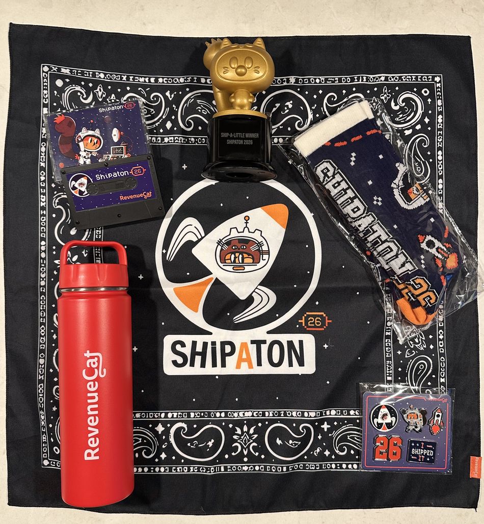 The Shipaton 2026 prize haul laid out on a black Shipaton bandana: a gold cat trophy engraved Ship-a-little Winner Shipaton 2026, a red RevenueCat water bottle, a Shipaton cassette-shaped sticker pack, navy Shipaton socks, and a set of enamel pins including one reading I Shipped It.